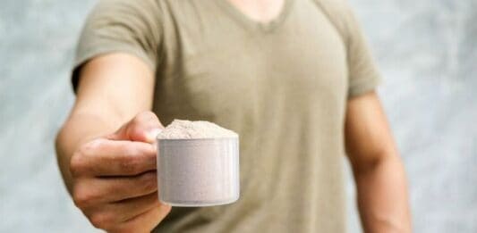 Tomar Whey Protein antes de Dormir ajuda no Ganho de Massa Muscular? Pessoa segurando colher de whey protein em pó, foco na proteína.