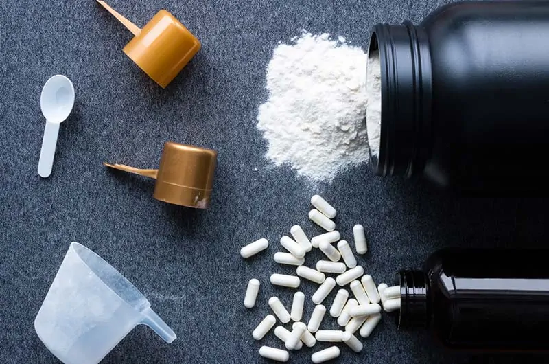 Suplemento de proteína em pó com cápsulas e colher para treinos.