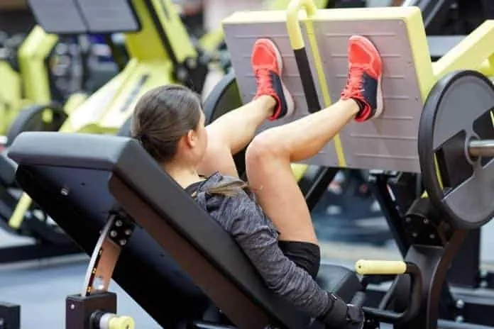 Mulher realizando exercício de leg press na academia.