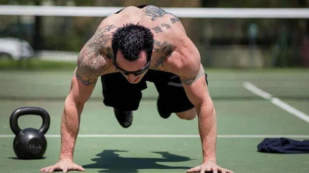 Homem realizando flexões de braços em treino ao ar livre.