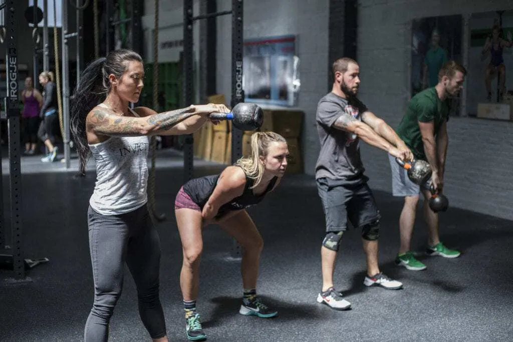 Mulheres e homens realizando exercícios de Crossfit com kettlebells.