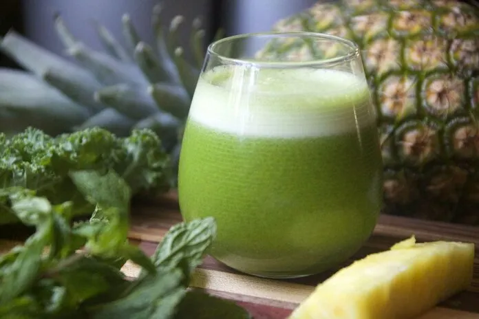 Suco detox para emagrecer rápido Suco detox verde em copo com abacaxi e hortelã ao fundo.