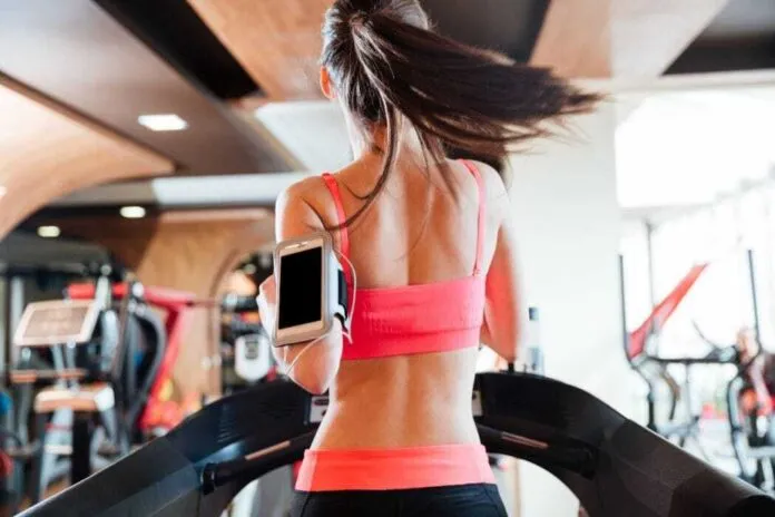 Mulher Correndo na Esteira para HIIT Mulher treinando HIIT na esteira com smartphone no braço.