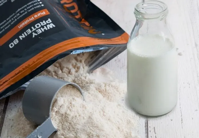 Whey Protein com Leite ou Água Whey protein em pó, leite e copo com leite em uma superfície de madeira.