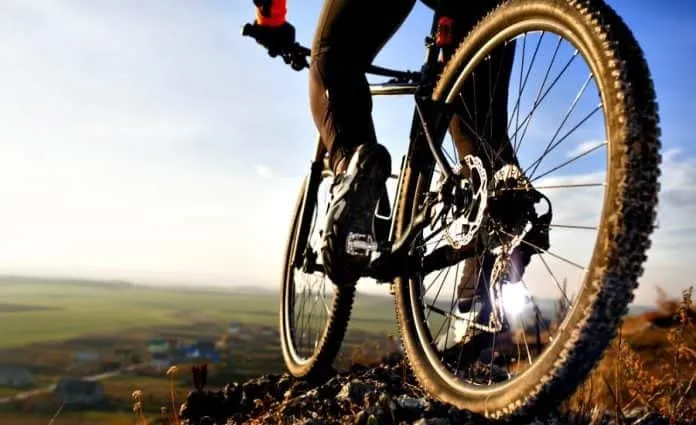 Benefícios de andar de bicicleta Pessoa pedalando bicicleta em trilha ao ar livre ao pôr do sol.