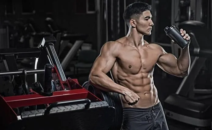 Homem musculoso bebendo água após treino na academia.