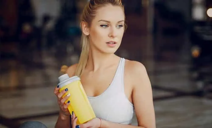 Mulher segurando garrafa de whey protein em academia.