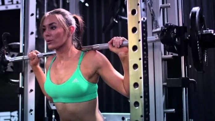Mulher fazendo agachamento na academia Mulher treinando agachamento na academia com barra e peso.