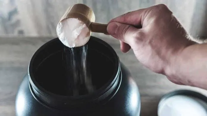 Tomar glutamina antes de dormir Pessoa adicionando glutamina em pó em um recipiente preto.
