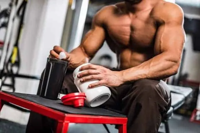 Homem musculoso preparando suplemento de proteína no ginásio.