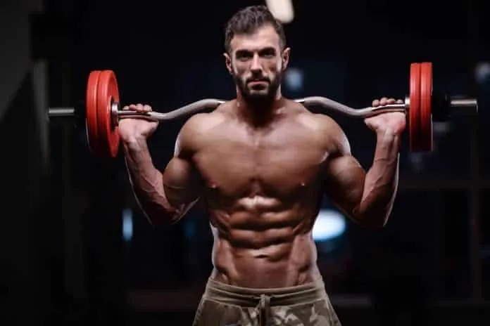 Homem treinando com halteres para hipertrofia Homem musculoso levantando halteres em treino de força.