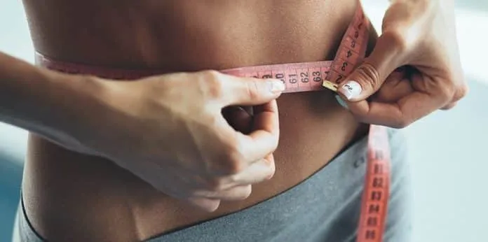 Medição da cintura para perda de peso Pessoa medindo a cintura com fita métrica para emagrecimento.