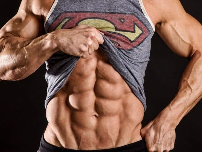 Definição muscular com GH Homem musculoso mostrando definição abdominal e usando camiseta do Superman.