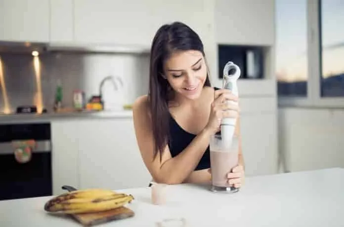 Bebida de proteína para treino Mulher preparando shake de proteína em cozinha moderna.