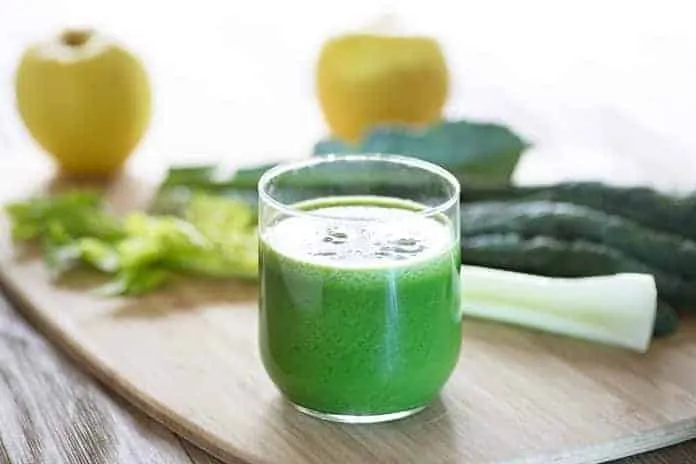 Suco detox de couve para emagrecer Suco detox de couve em copo transparente com ingredientes ao fundo.