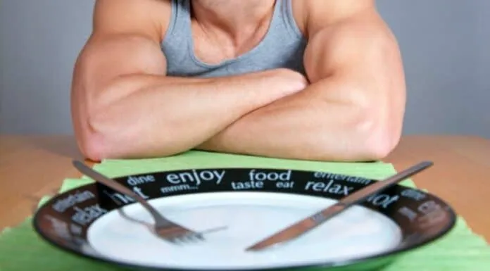 Homem com braços musculosos e prato vazio Homem com braços musculosos e prato vazio na mesa.