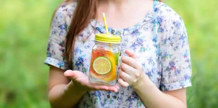 Bebida detox com limão e frutas Mulher segurando jarra com limão, frutas e água detox.