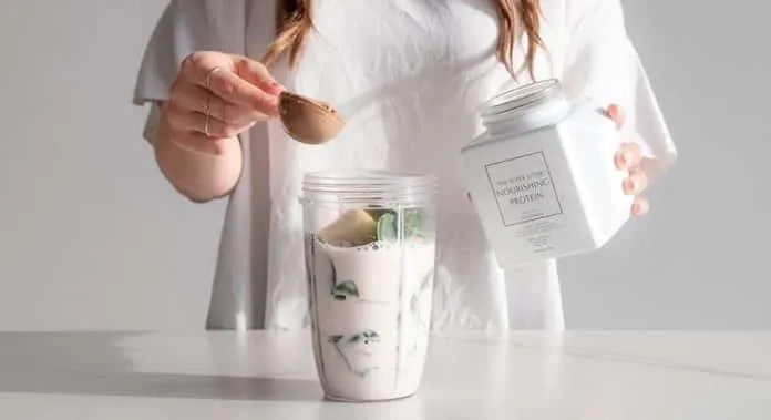 Pessoa adicionando pó de proteína a um shake de iogurte.