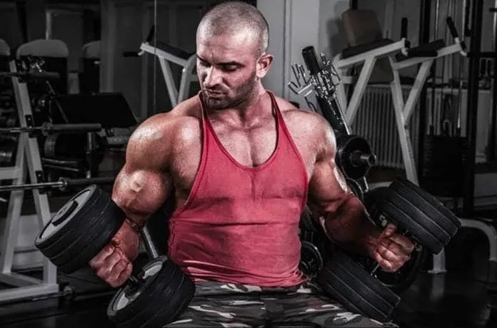 Homem treinando com halteres em academia Homem musculoso treinando com halteres em academia.