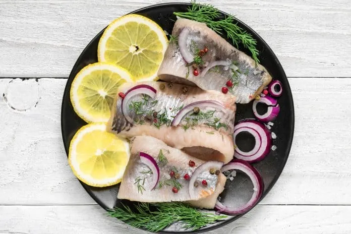 Sardinha fresca com limão e ervas Sardinha fresca com limão, cebola e ervas em prato preto.