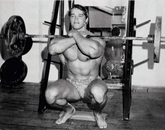 Treino de Pernas do Arnold Schwarzenegger Arnold Schwarzenegger fazendo agachamento com barra na academia.