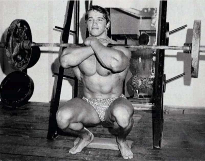 Arnold Schwarzenegger fazendo agachamento com barra pesada.