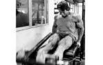 Arnold Schwarzenegger treinando pernas com peso livre em academia.