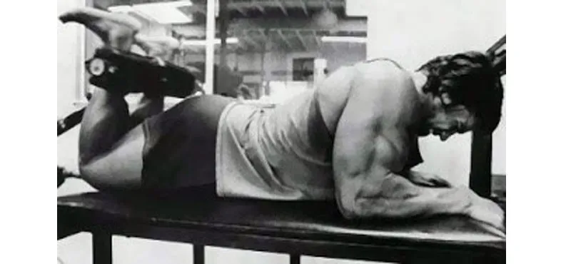 Arnold Schwarzenegger realizando exercício de pernas avançado.