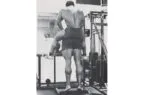 Arnold Schwarzenegger treinando pernas com parceiro no ginásio.