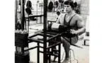 Arnold Schwarzenegger treinando pernas com halteres na academia.