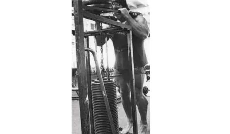 Homem treinando pernas com peso em academia.