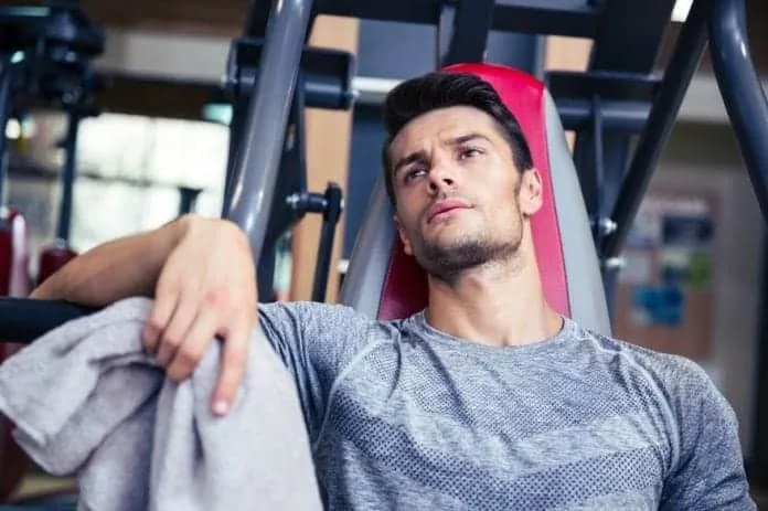 Homem pensativo descansando na academia após treino intenso.
