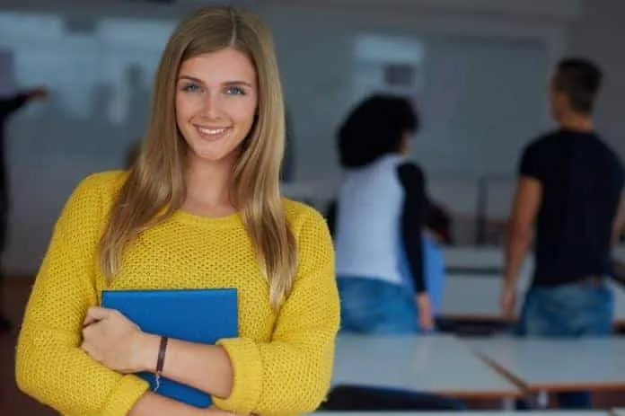 Jovem estudante sorridente com caderno azul Jovem estudante sorridente segurando caderno azul em ambiente escolar.