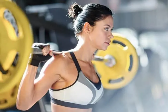 Treino de Pernas com Carol Saraiva Mulher treinando pernas com barra em academia.
