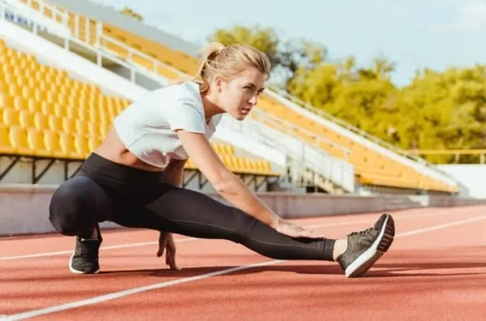 Mulher fazendo alongamento na pista de corrida ao ar livre.