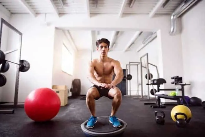 Homem treinando em academia com equipamentos de musculação e peso.