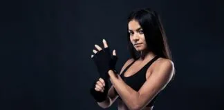 Mulher fitness com luvas de treino, vestindo roupa esportiva preta.