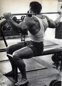 Homem treinando abdômen com barra em academia, foco em músculos abdominais e costas.