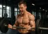 Dra. Samira: 5 exercícios para Aumentar a Testosterona Homem musculoso fazendo exercício com halteres na academia.